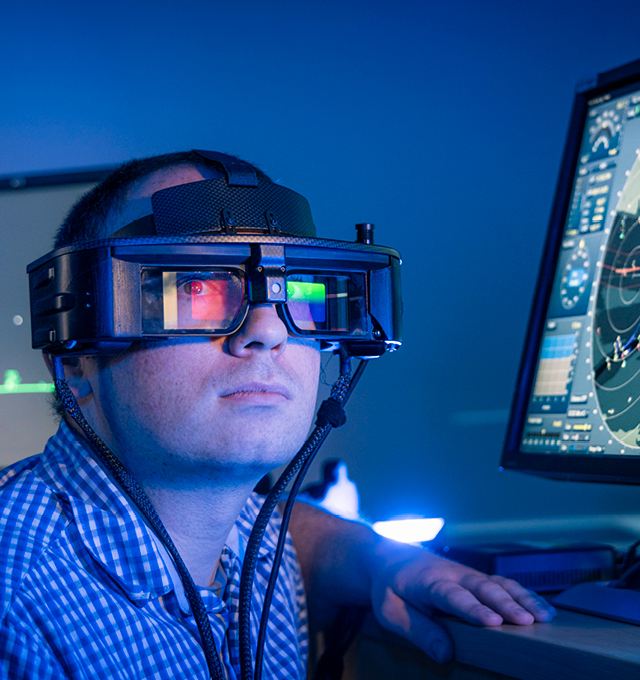 A BAE System employee wearing a headset with a computer screen in the background