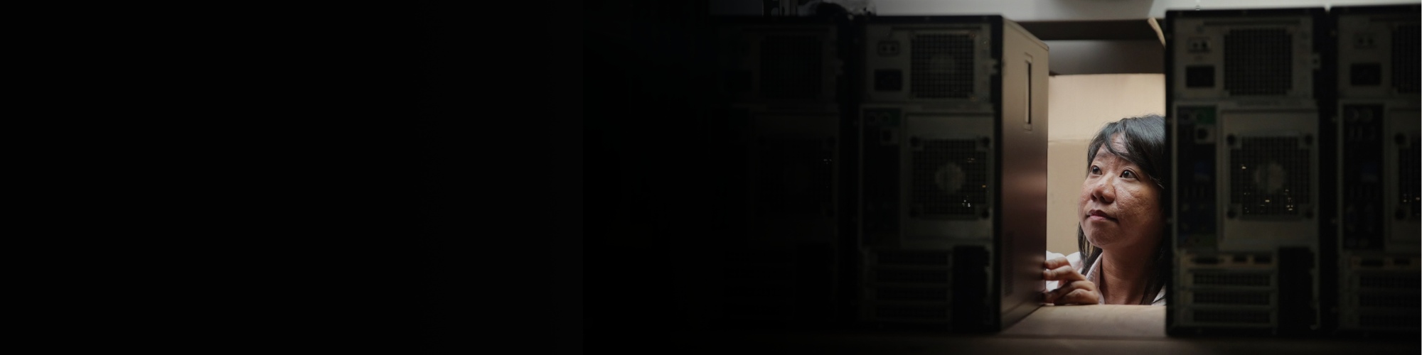 A BAE Systems employee examines a computer in a server room, surrounded by rows of servers.