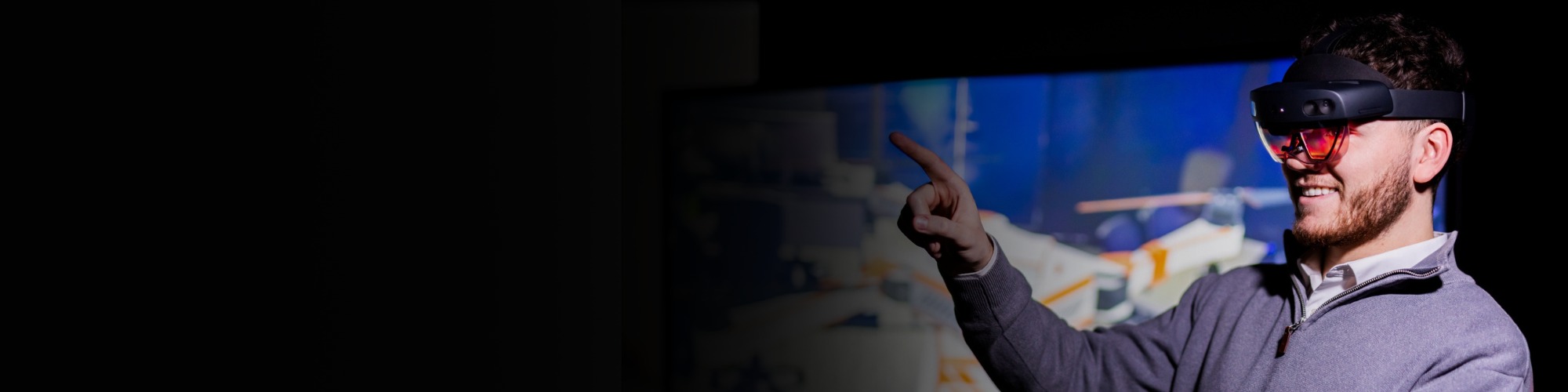 A BAE Systems employee in virtual reality glasses points at a screen.