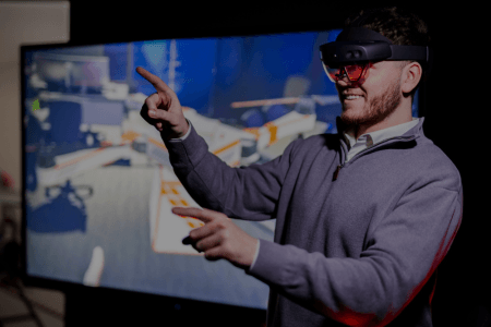 A BAE Systems employee in virtual reality glasses points at a screen.