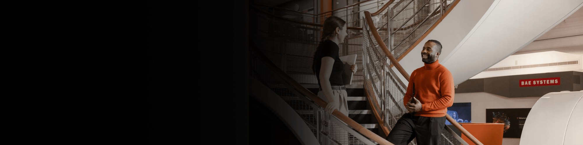 Two PMs standing on the stairs at BAE Systems, engaged in conversation.