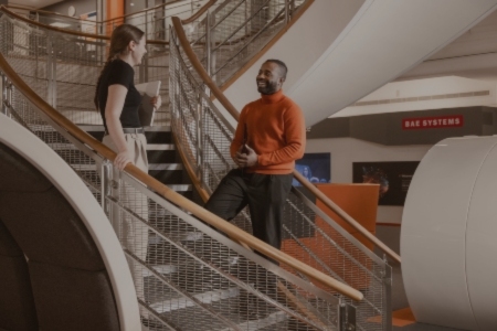 Two PMs standing on the stairs at BAE Systems, engaged in conversation.