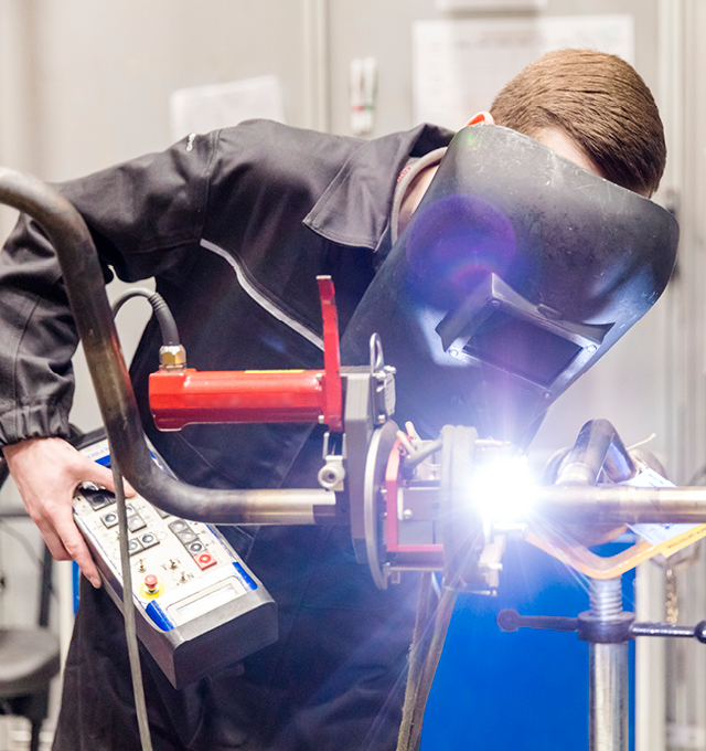 A BAE Systems employee in a welding suit working on welding a metal object