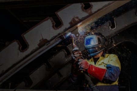 A welder in a helmet holds a torch, showcasing the manufacturing process at BAE Systems.