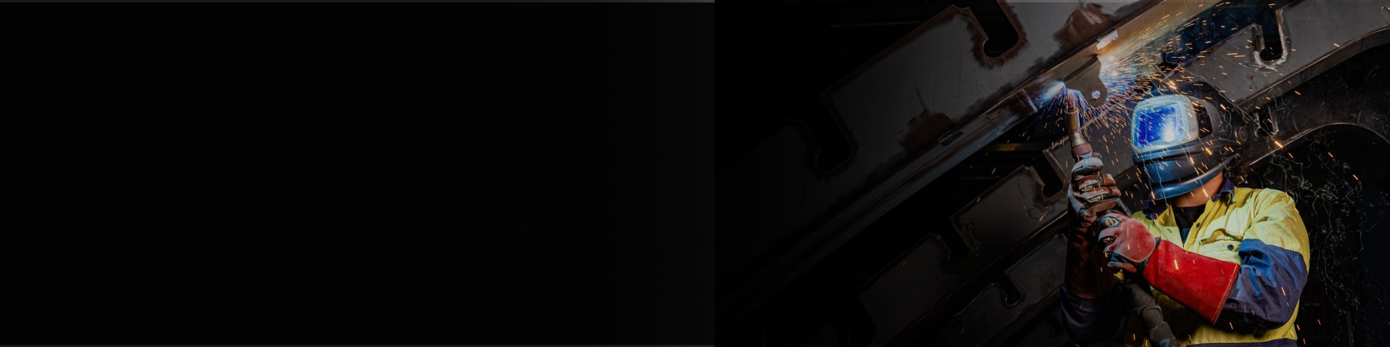 A welder in a helmet holds a torch, showcasing the manufacturing process