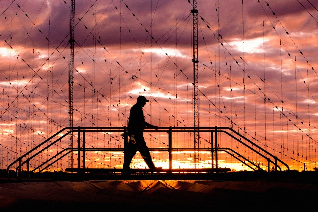 An engineer at BAE Systems walks across Jindalee Operational Radar Network during sunset, with vibrant orange and purple hues in the sky.