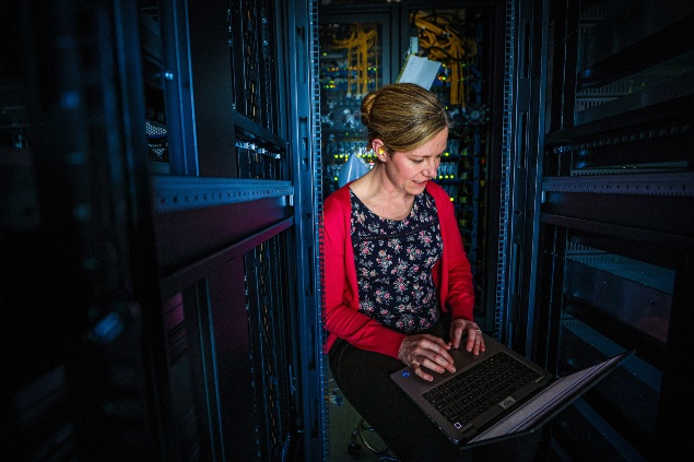 Female seated in a server room, focused on her laptop amidst rows of BAE Systems servers and equipment.