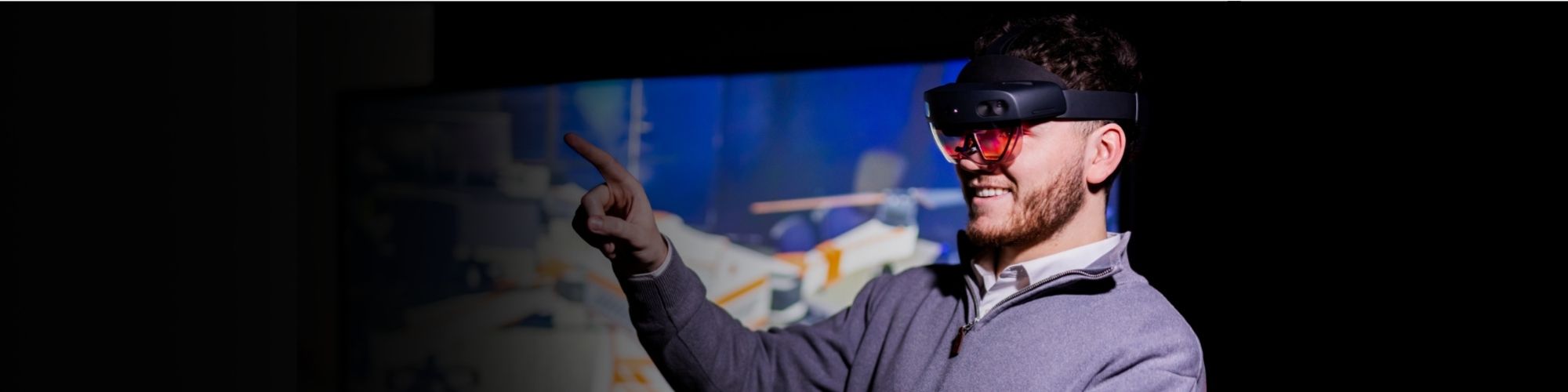 An engineer at BAE Systems wearing goggles and pointing at a screen